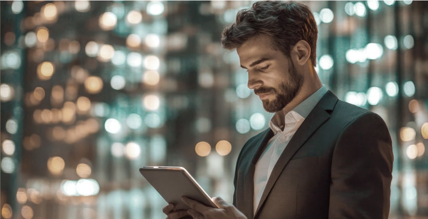 Homem de terno usando um tablet em frente a um prédio iluminado